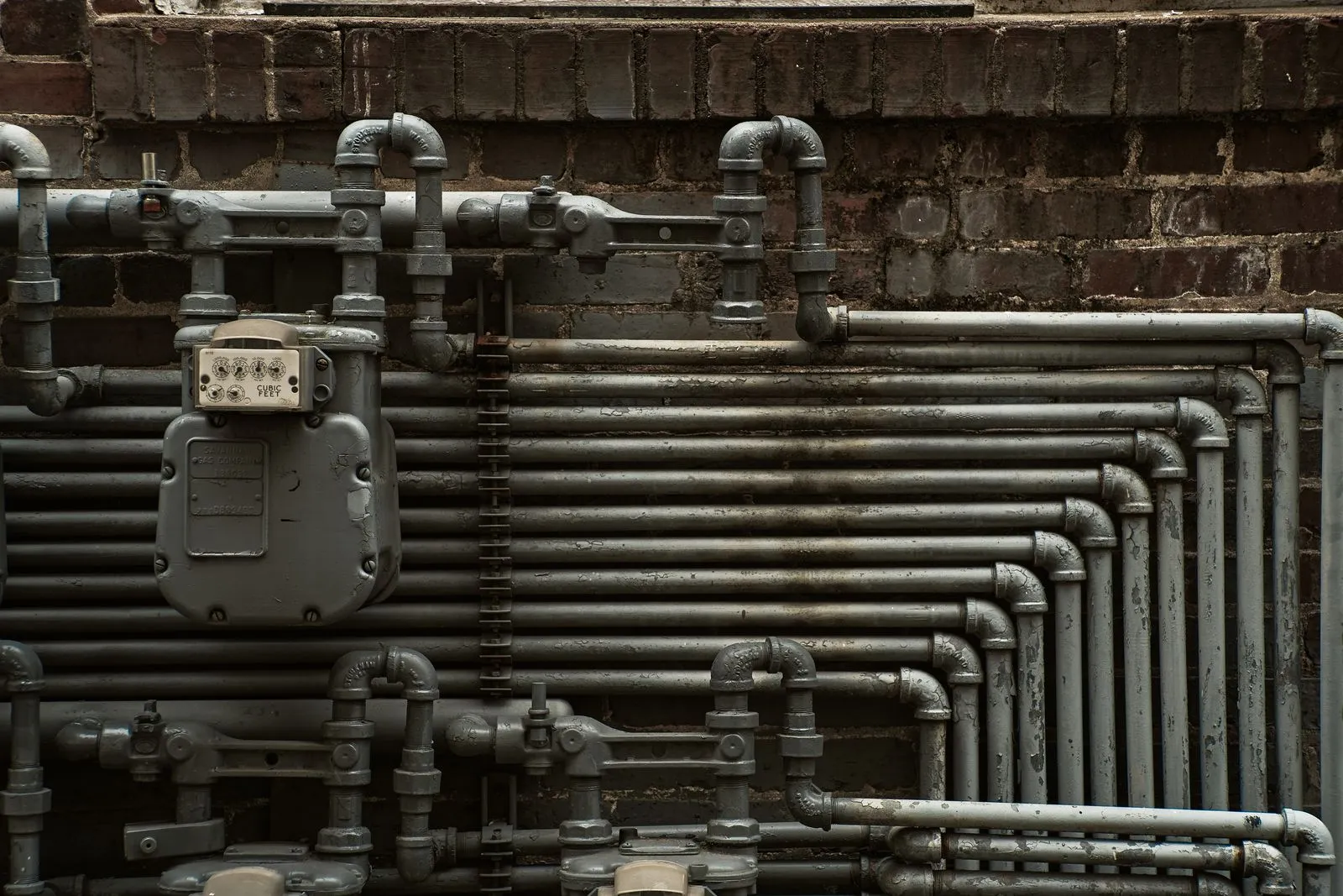 Close-up of industrial steel pipes and a gas meter on a brick wall