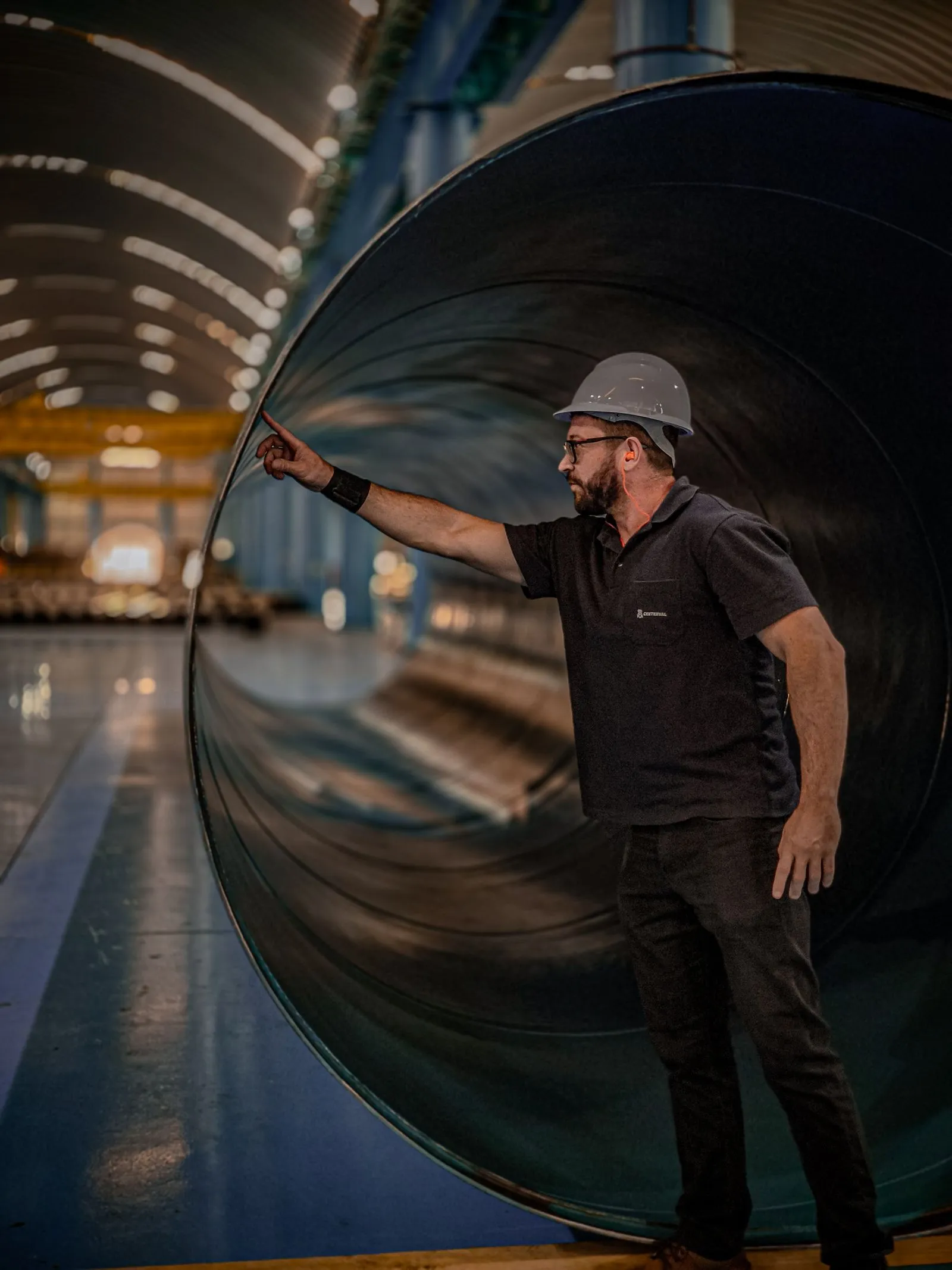 Engineer in a safety helmet assessing a large steel pipe in a manufacturing warehouse